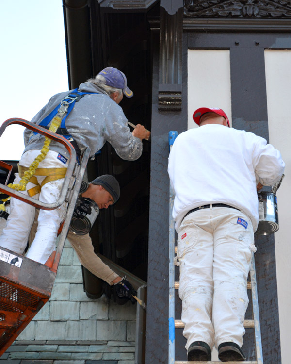 Three men painting exterior of home while on lift